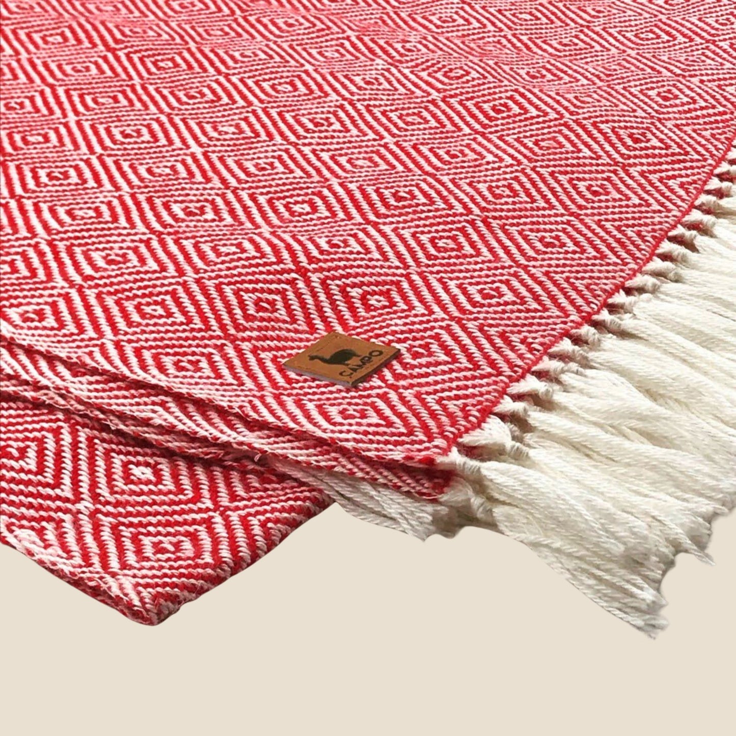 Red and white patterned blanket with a brand logo on a beige background