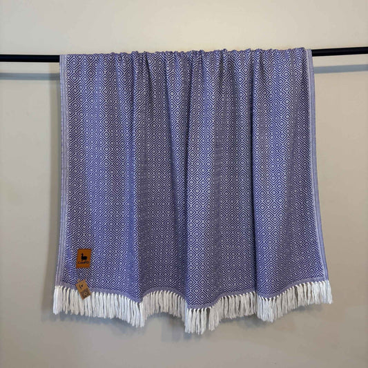 Purple patterned towel with white fringe draped over a black rod against a beige wall.