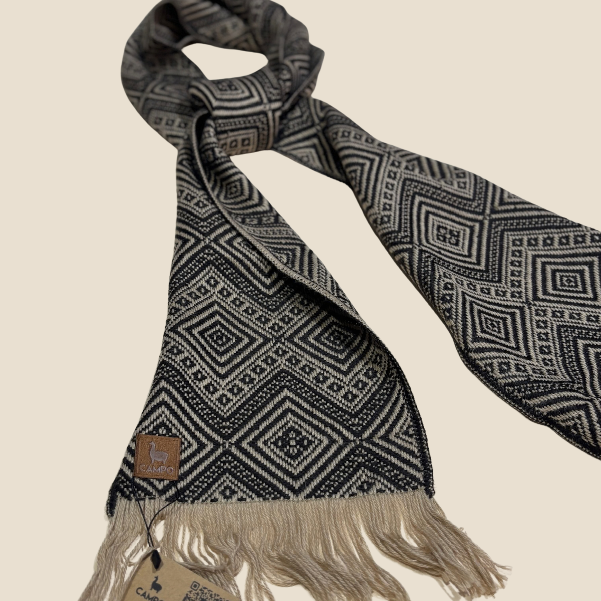 Patterned scarf with fringes and a brand tag on a beige background