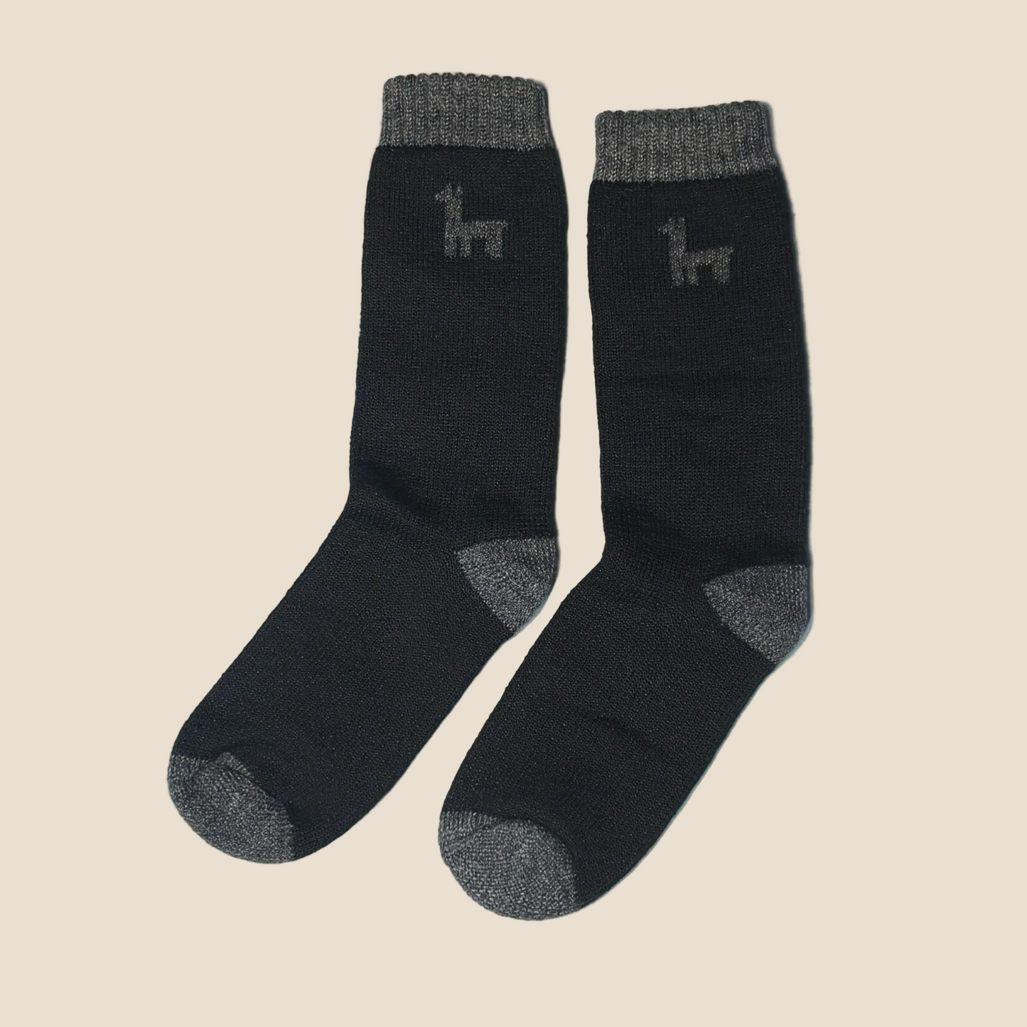 A pair of dark charcoal gray knit socks with lighter gray ribbed cuffs, heels, and toes, featuring a small stylized llama logo on the upper calf, displayed on a solid light beige background.