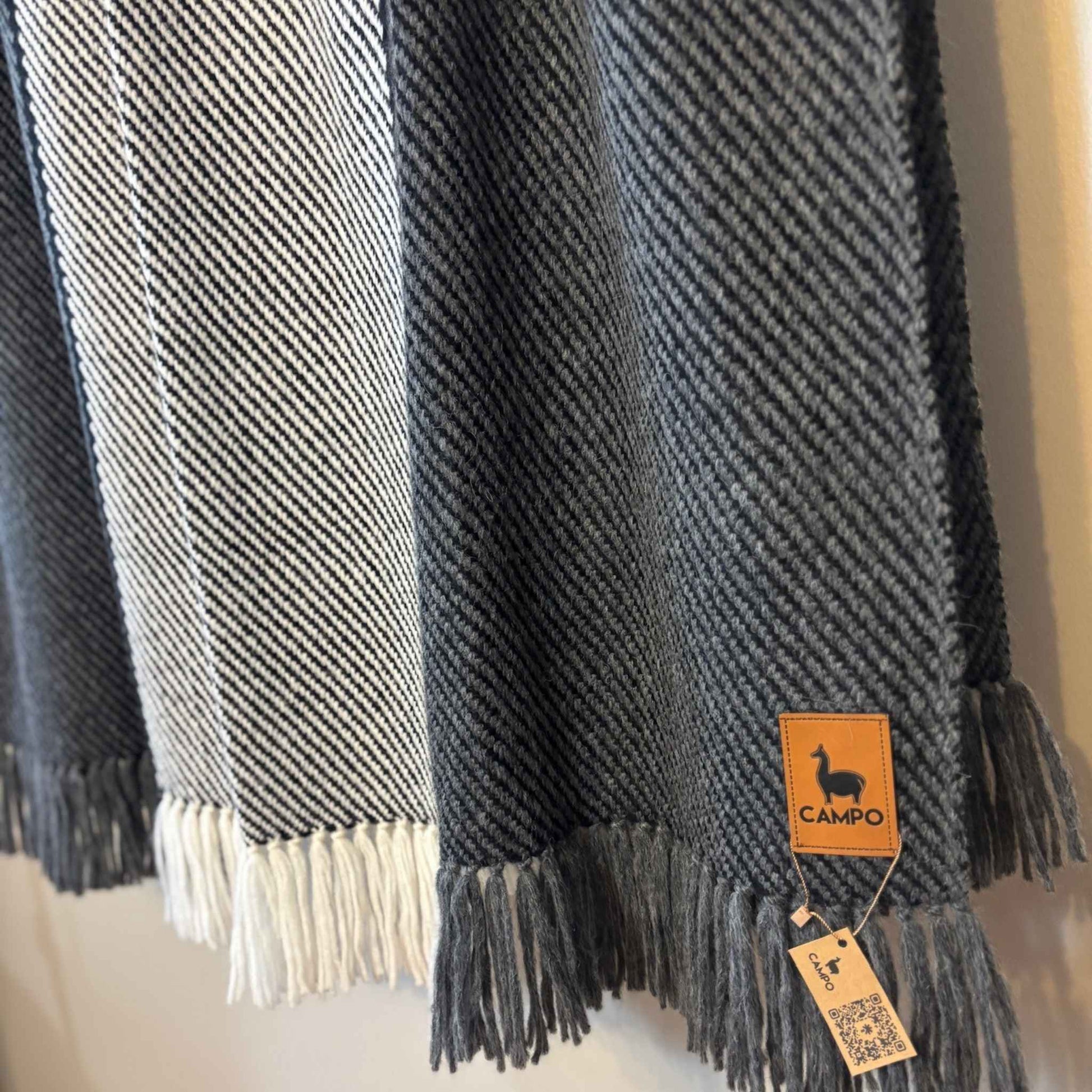 Charcoal woven blanket with tassels and a 'Campo' brand tag on a neutral background