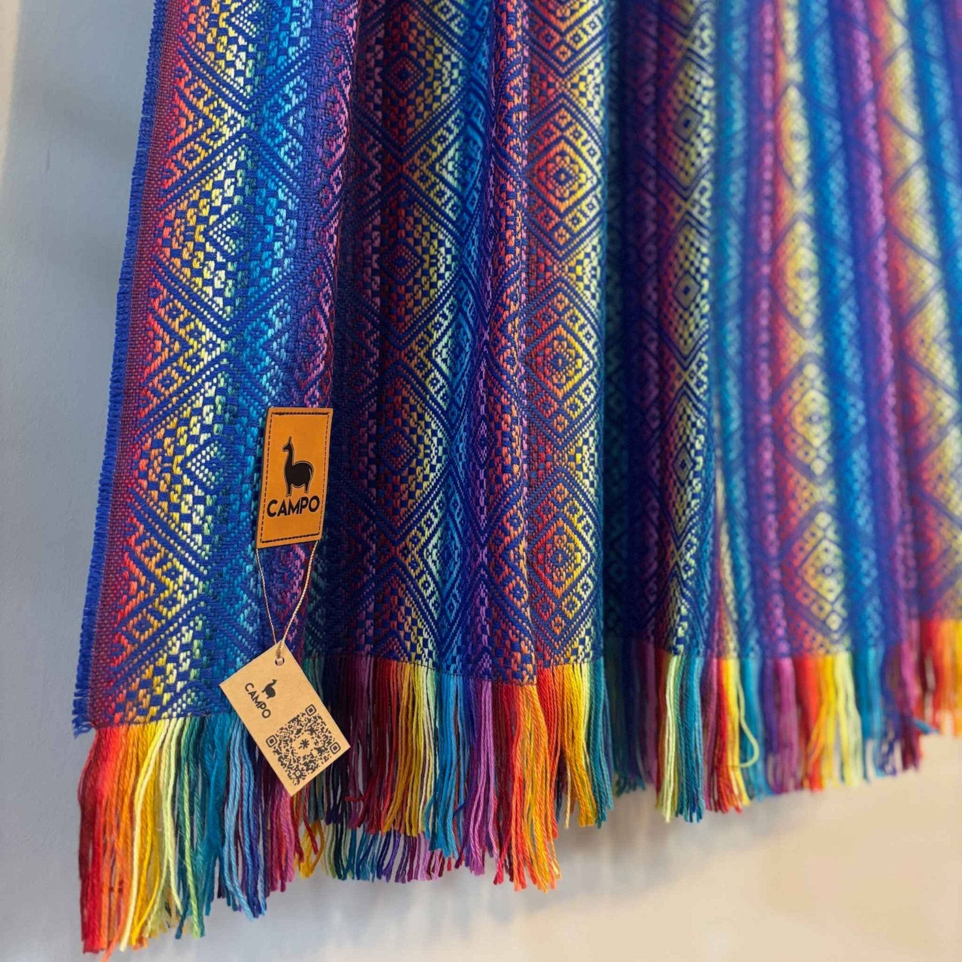 Blue rainbow patterned fabric with tassels and a visible brand tag on a neutral background
