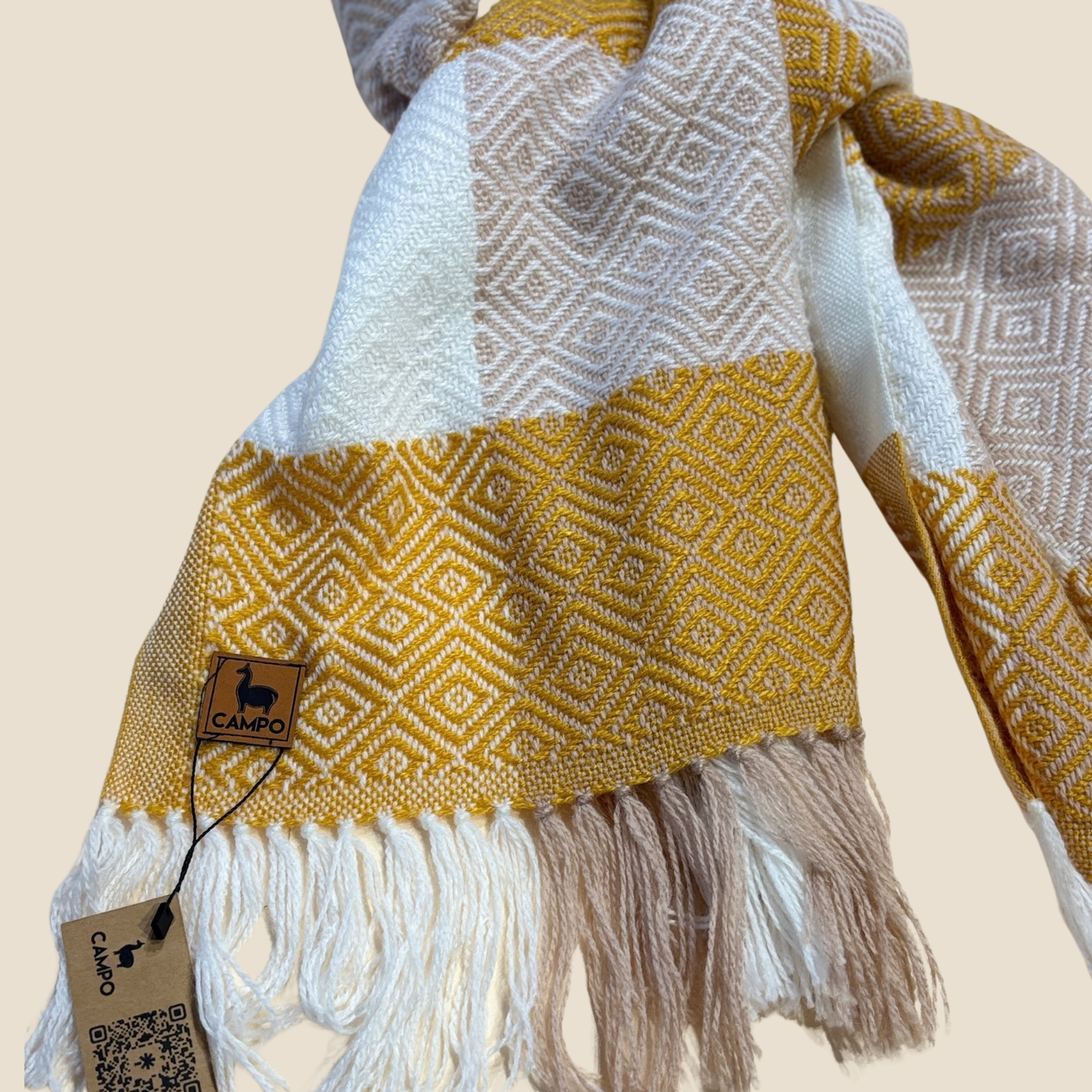 Yellow and white patterned scarf with fringes and a visible brand tag on a beige background