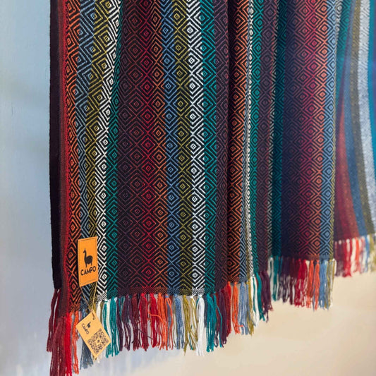 Black multi woven blanket with geometric patterns and fringes on a light background