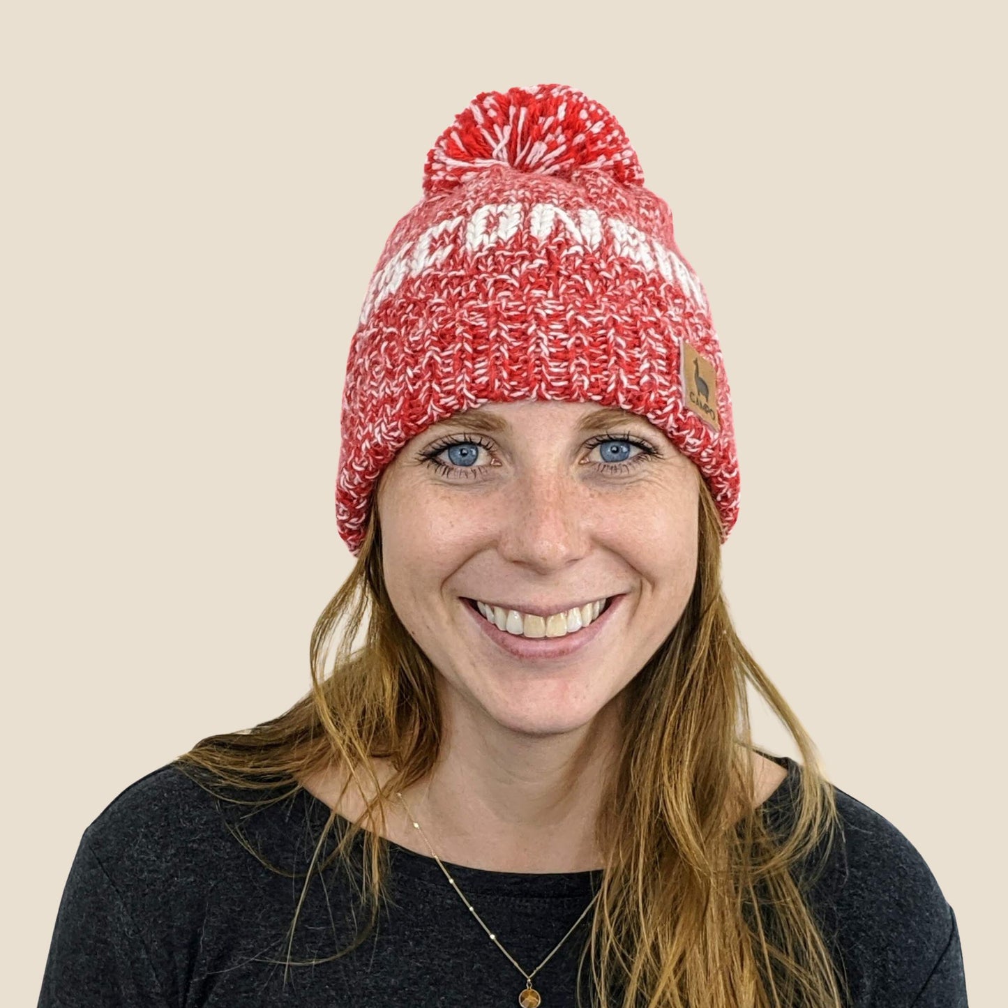 Person wearing a red and white knit beanie with a pom-pom on a beige background
