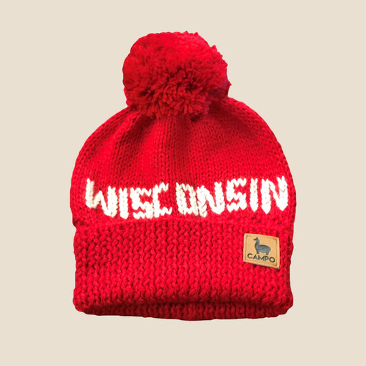 Red knit beanie with 'WISCONSIN' text and a pom-pom on a beige background
