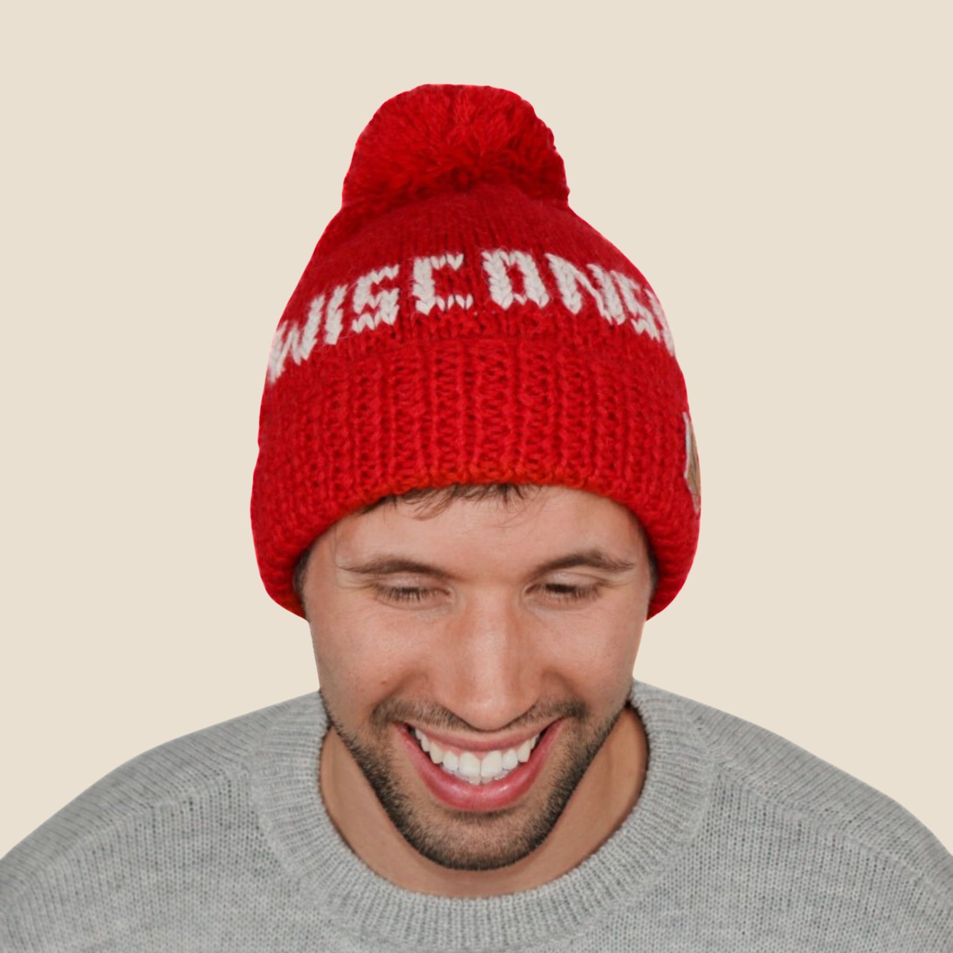 Person wearing a red 'Wisconsin' beanie on a beige background