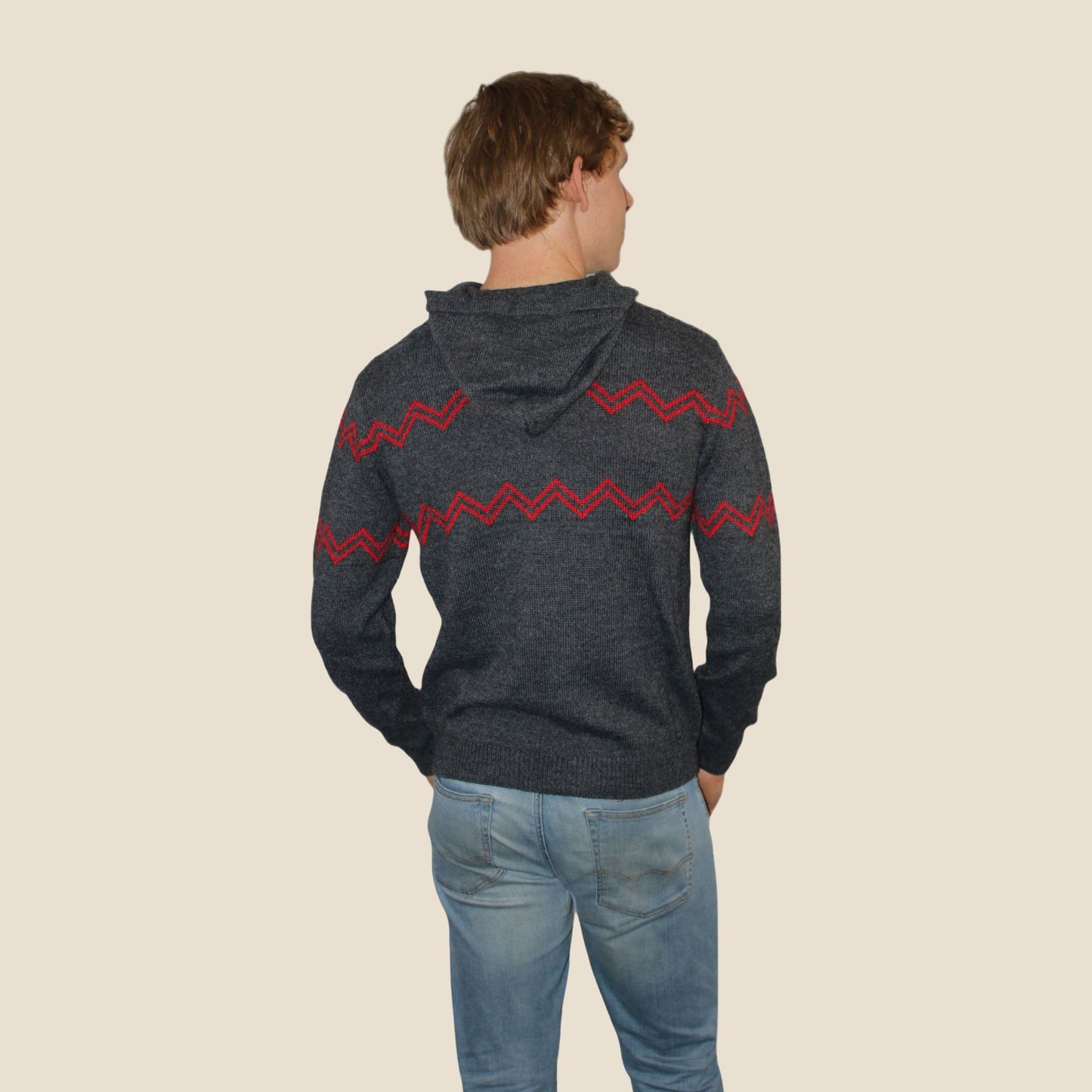 Person wearing a dark gray hoodie with red zigzag pattern on the back, standing against a beige background.