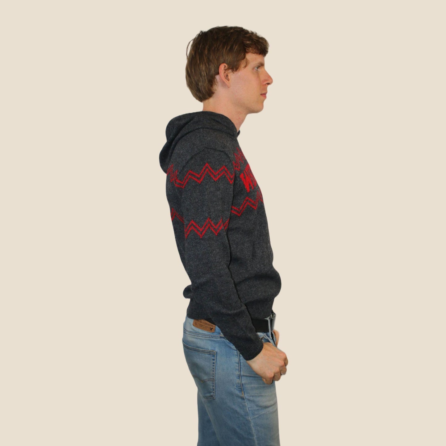 Person wearing a dark gray hoodie with red patterns on a beige background