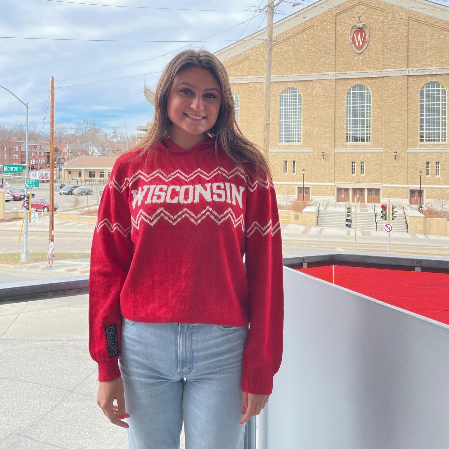 Person wearing a red 'Wisconsin' sweater standing in front of a building with a large 'W'.