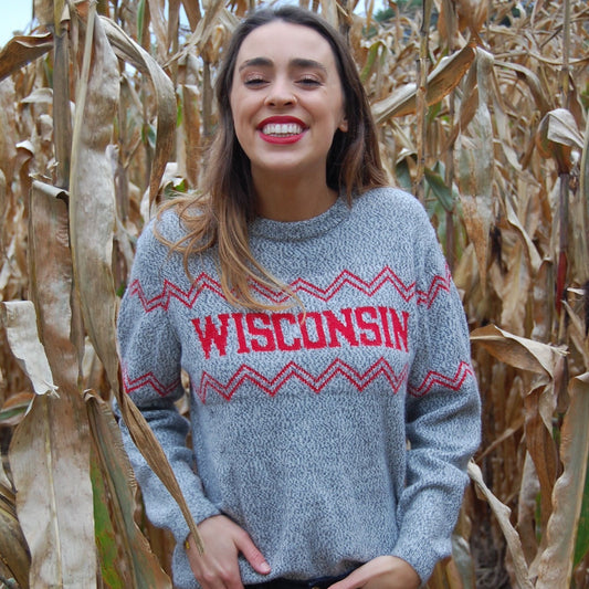 Woman wearing a gray sweater with 'Wisconsin' printed on it, standing in a cornfield.