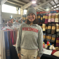 Woman wearing a 'Wisconsin' sweatshirt in a store with clothing racks and merchandise.