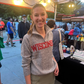 Woman wearing a 'WISCONSIN' sweater standing outdoors with people and booths in the background.