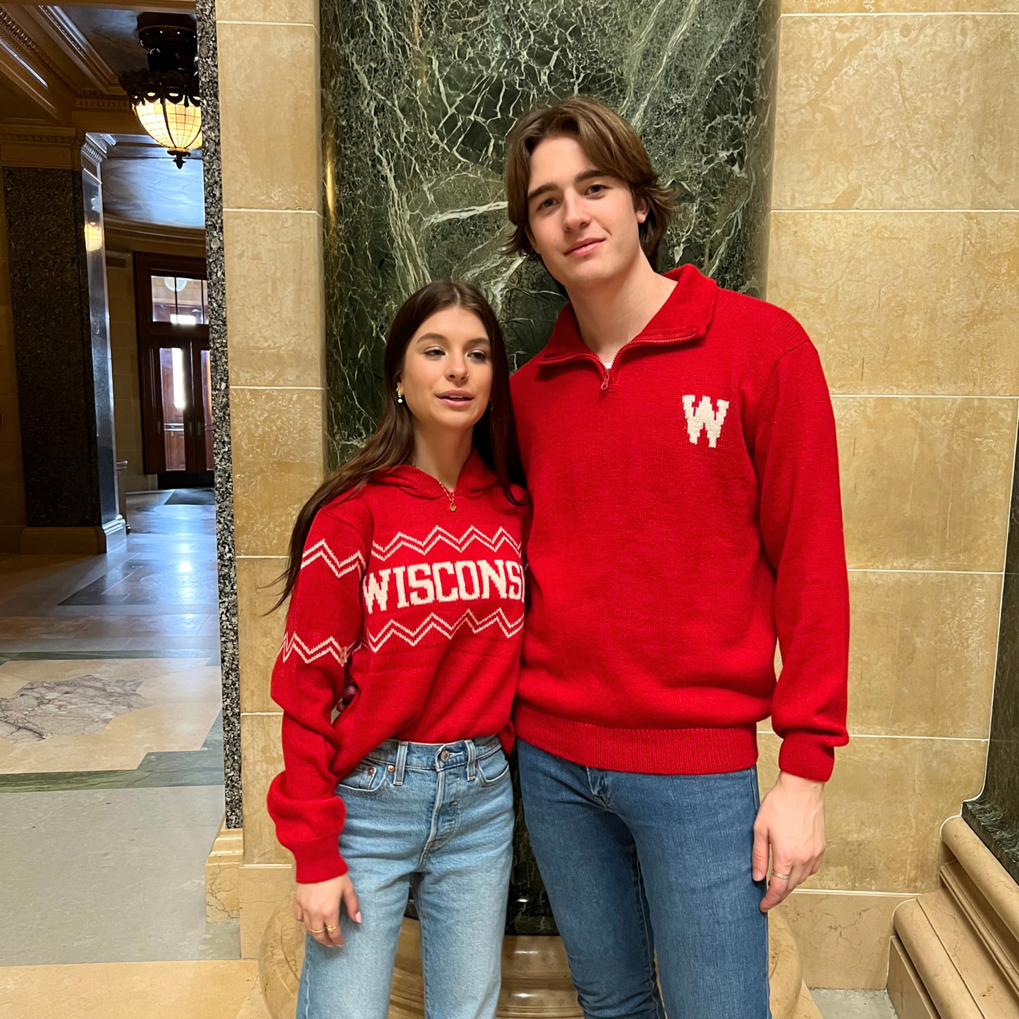 Two people wearing red 'WISCONSIN' sweatshirts in a marble hallway.
